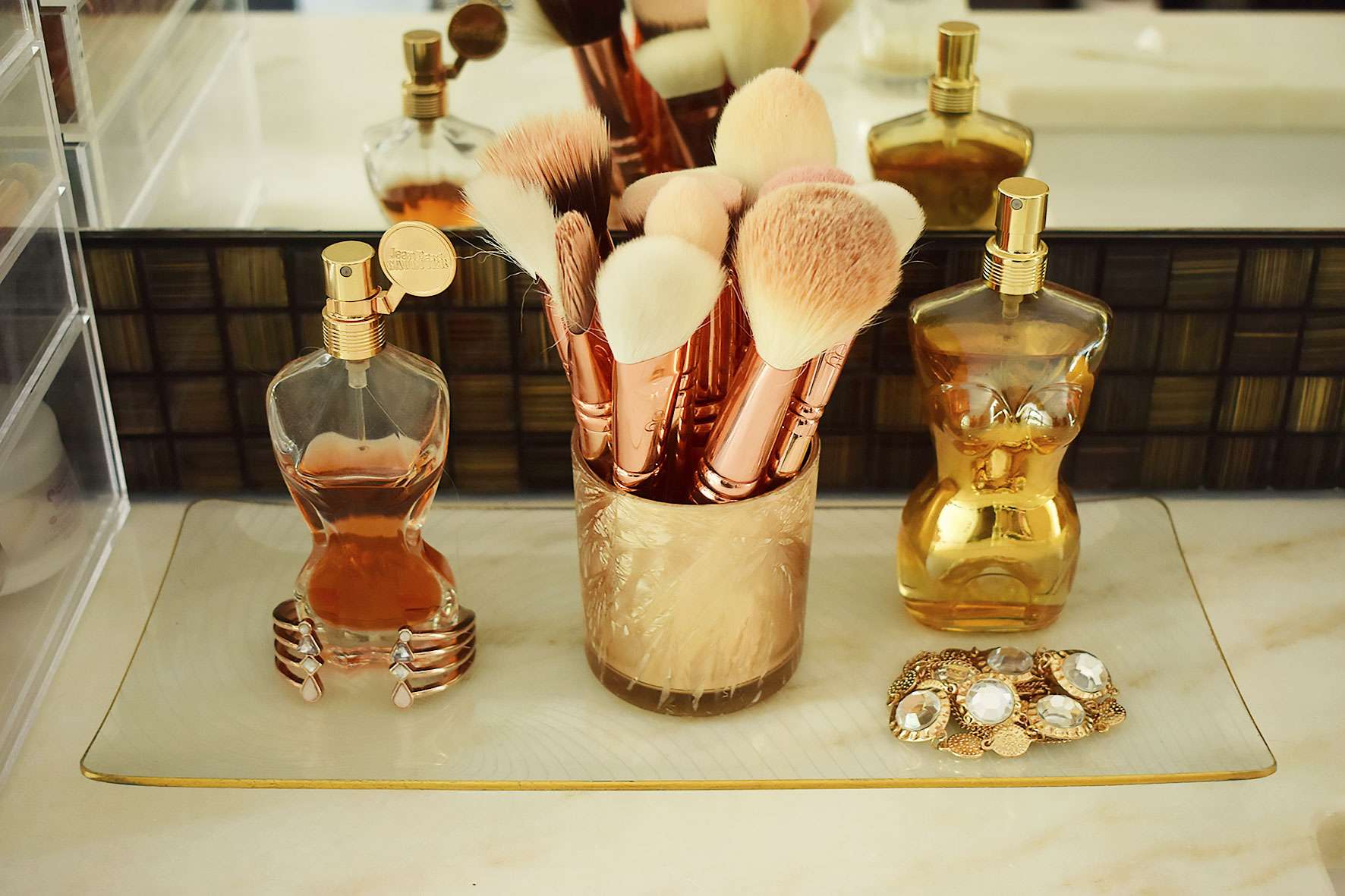 JPG perfume bottles and make up brushes on a glass tray