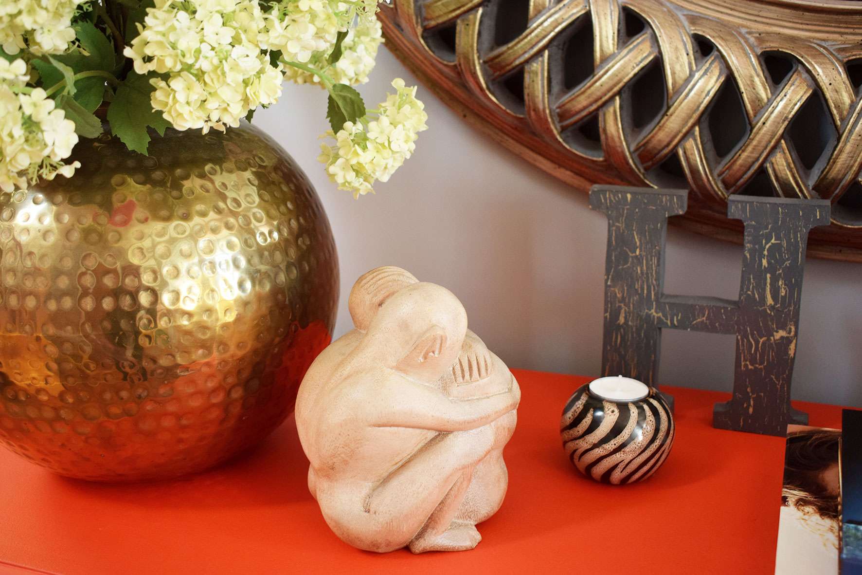 wooden lovers sculpture next to brass hammered globe vase full of flowers