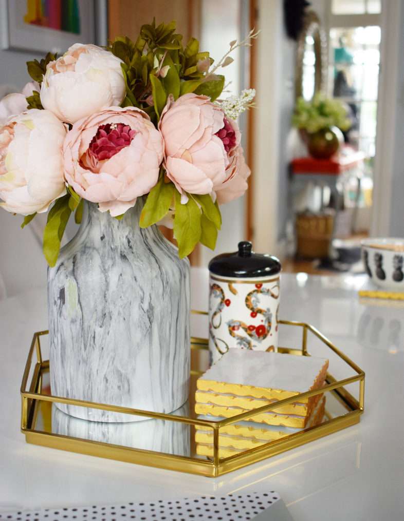 gold tray on table containing marble vase of blush peonies, candle, and marble coasters