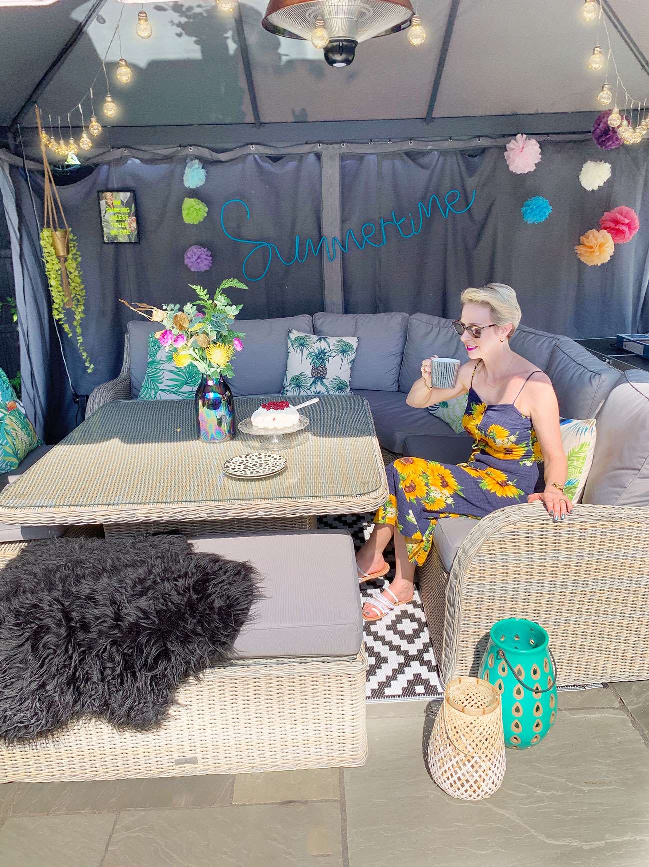 Woman sitting at table in colourfully decorated gazebo drinking tea.