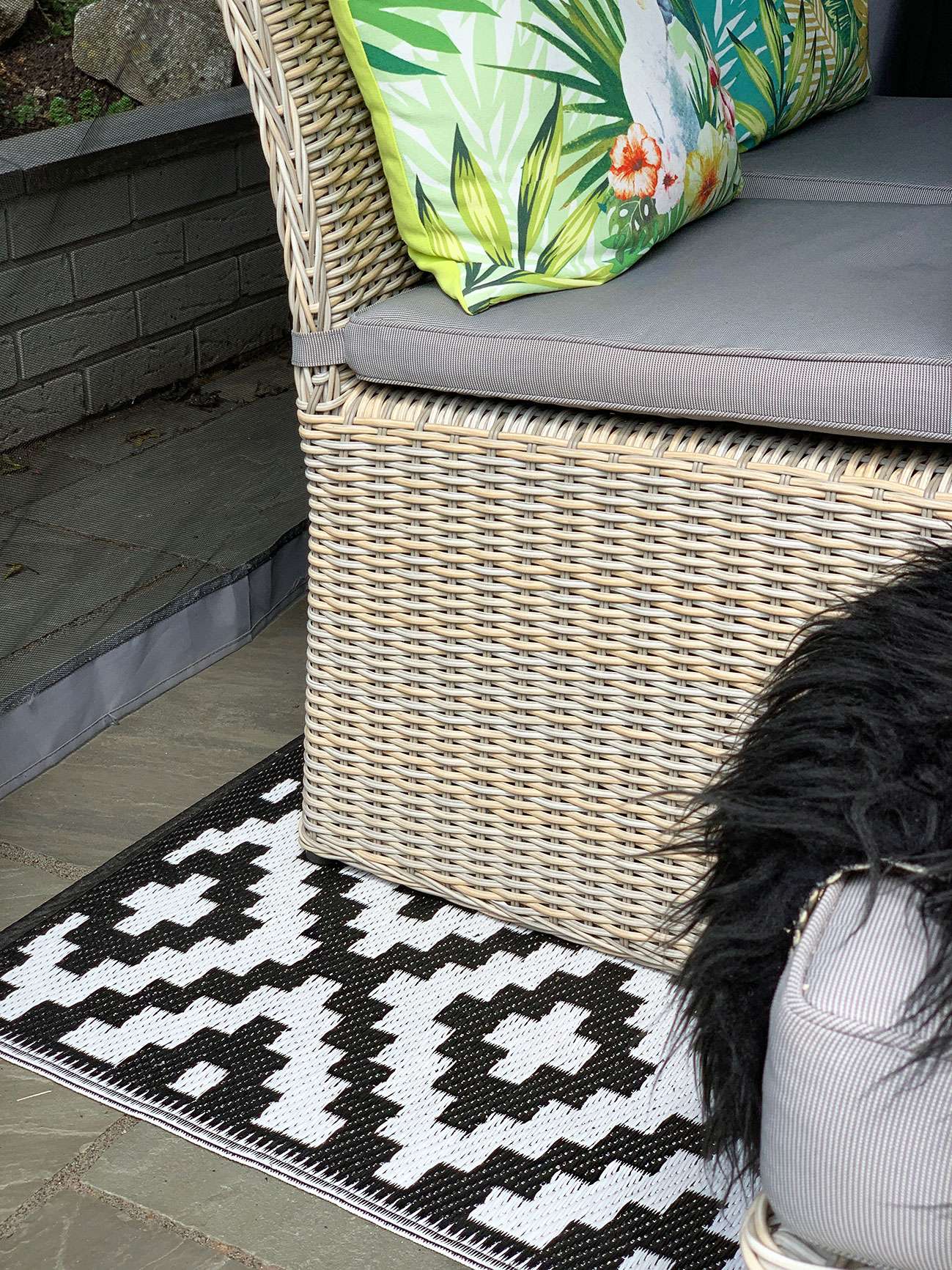 Patio rattan chairs with tropical cushions on a monochrome outdoor rug.