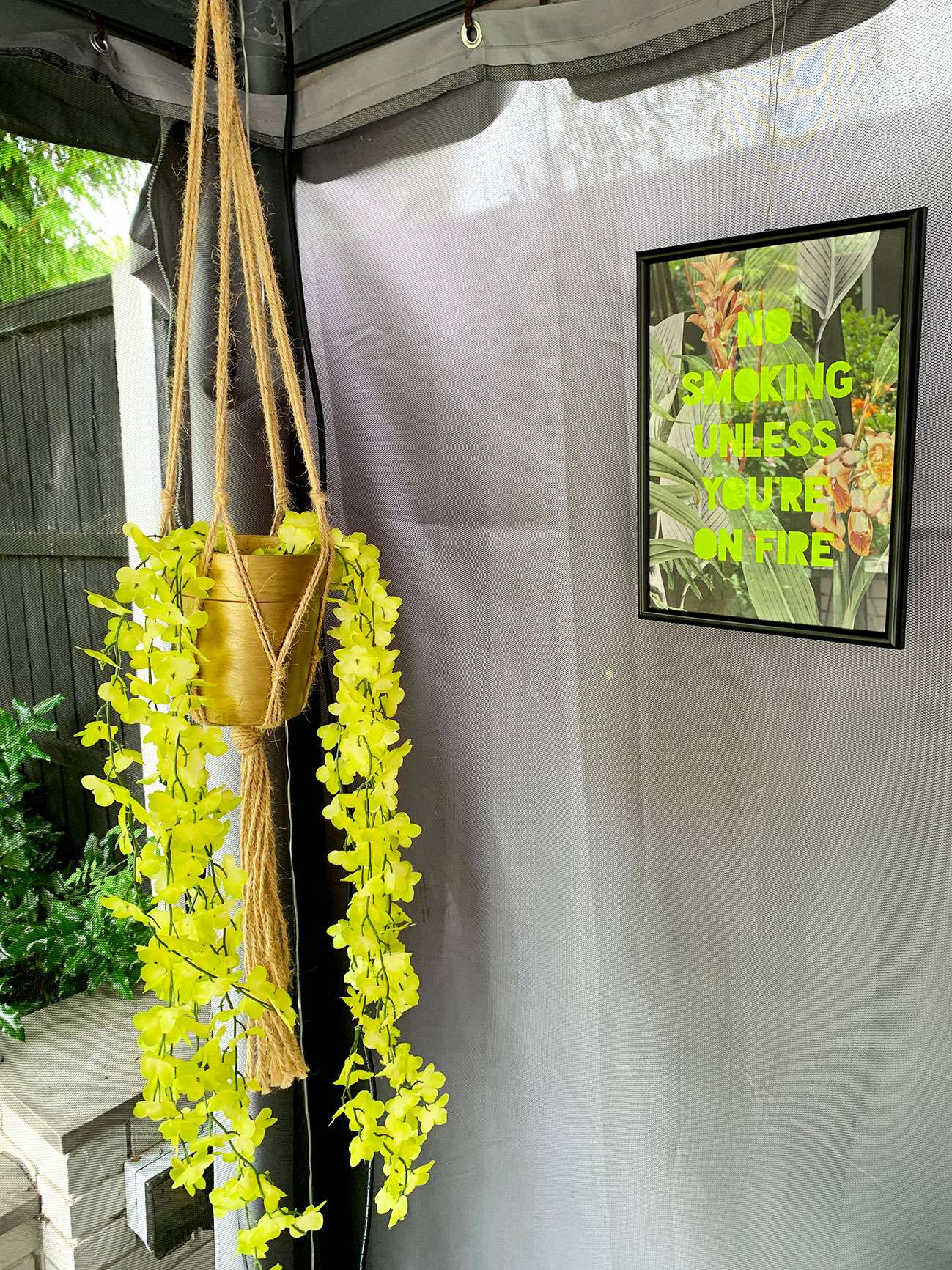 Macrame hanging with gold planter and trailing artificial plant next to 'no smoking unless you're on fire' decorative sign.
