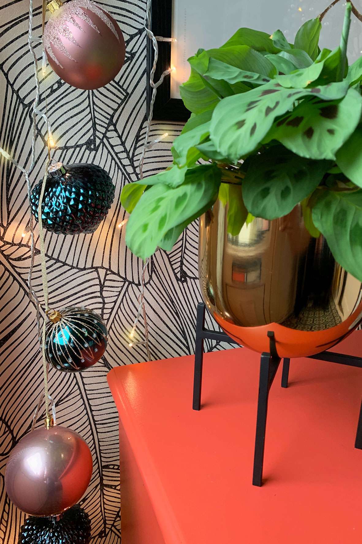 teal and blush pink Christmas hanging decoration next to a plant in a gold planter