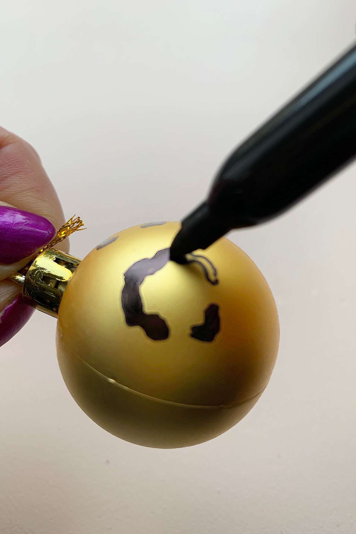 Someone colouring in a leopard spot on a gold Christmas bauble