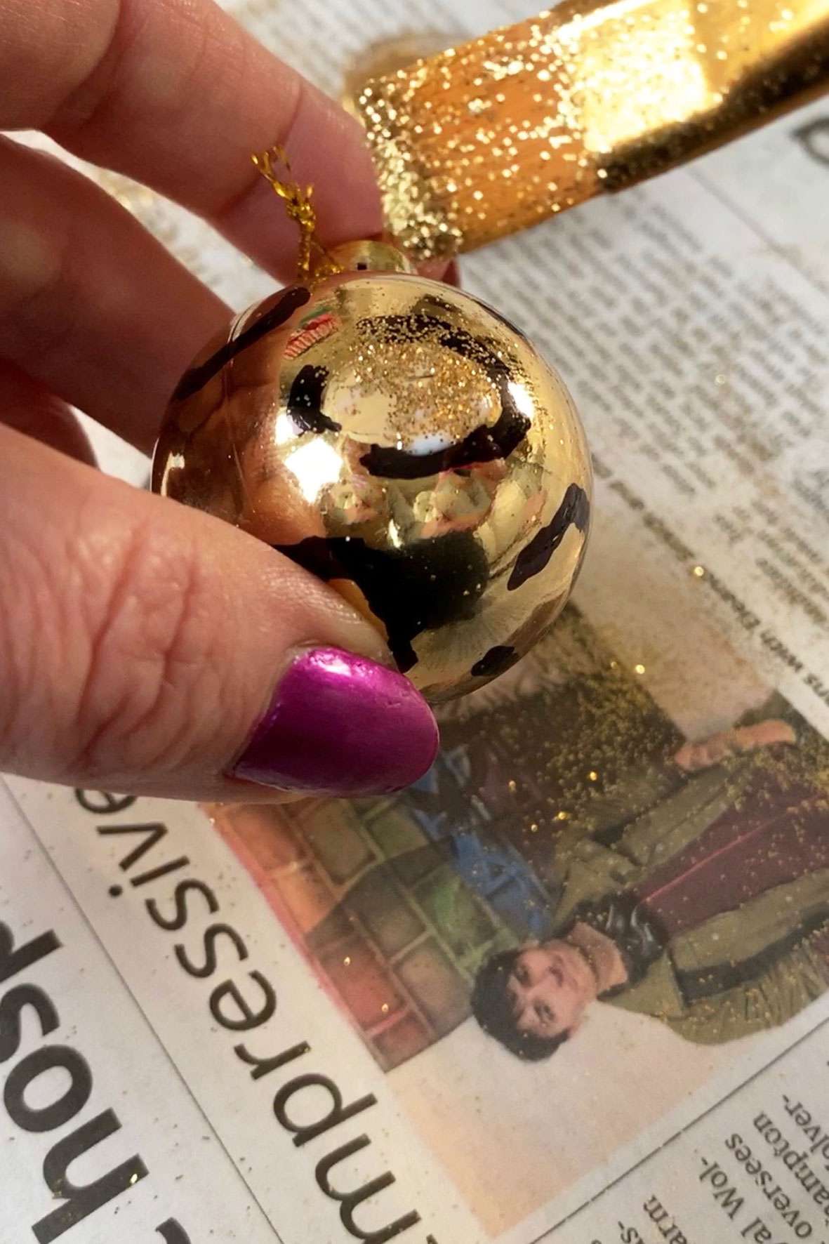 Someone decorating a gold bauble by sprinkling glitter onto it