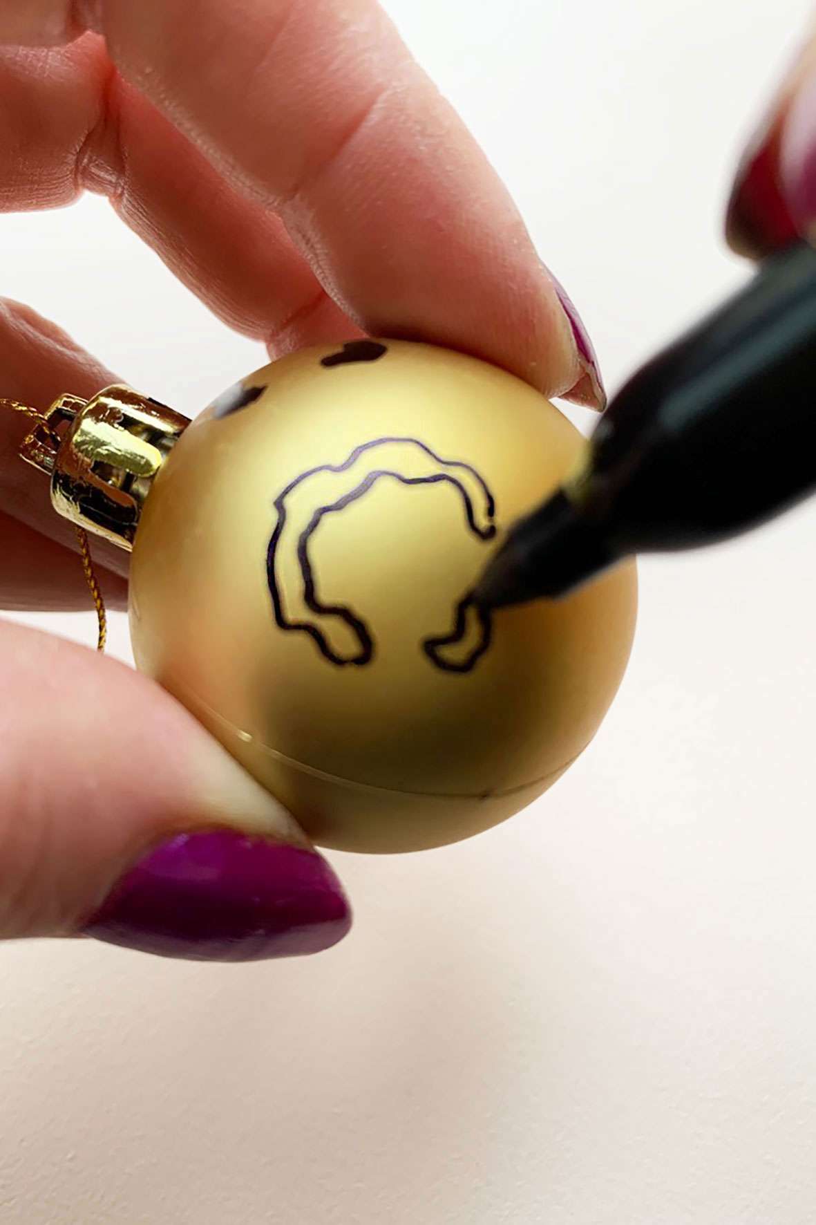 Someone drawing a leopard spot on a gold Christmas bauble