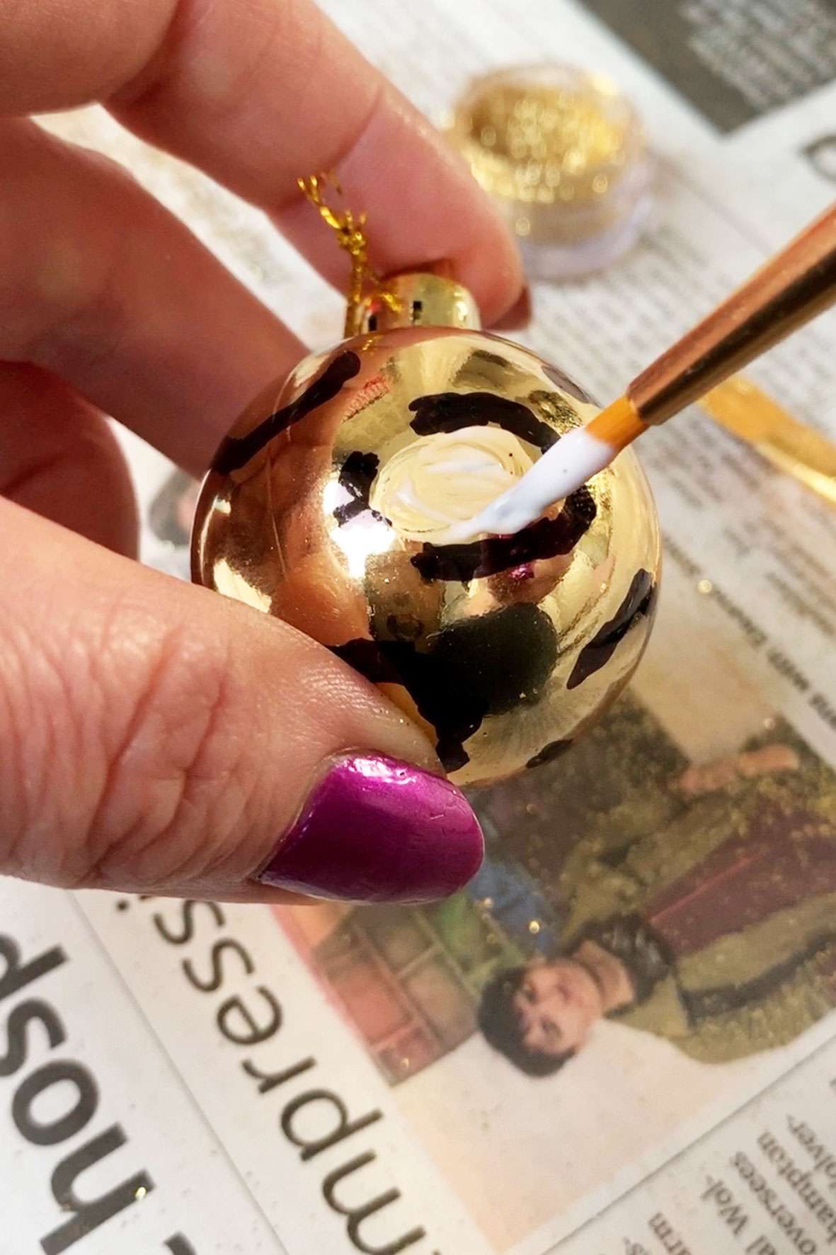 Someone decorating a gold Christmas bauble and painting PVA glue on 
