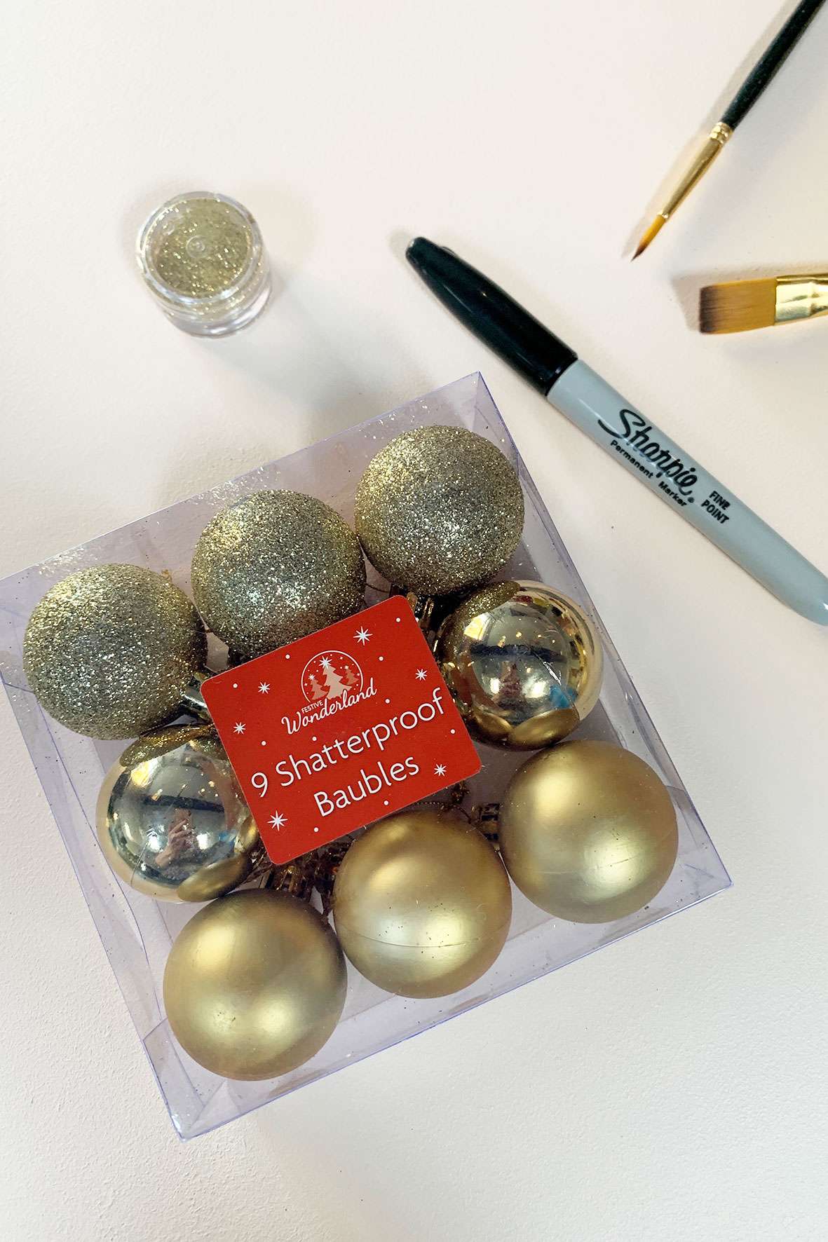 Flat lay of gold baubles, sharpie pen, glitter and brushes. 
