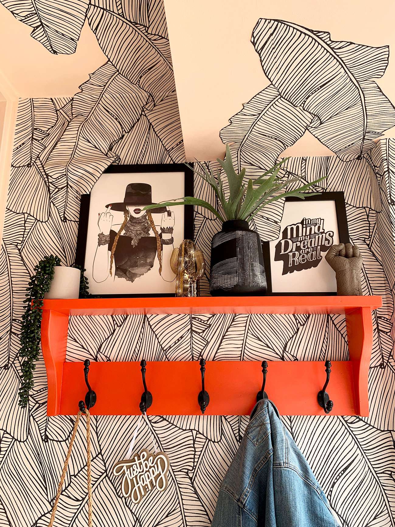 Coral coat hook on a monochrome palm leaf wallpapered wall and ceiling.