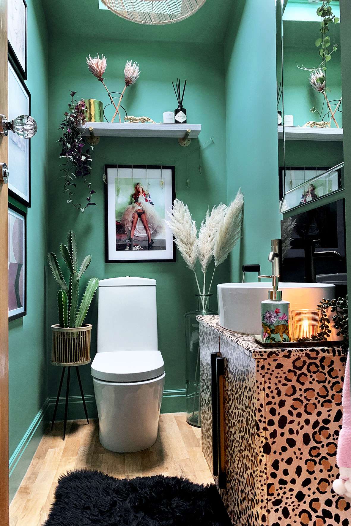 Toilet room with teal walls, Kate Moss print, pampas grass, and leopard print sink unit.