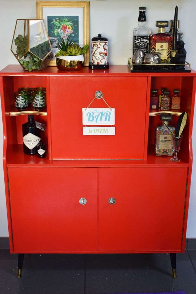 Red Upcycled vintage G Plan cocktail cabinet with alcohol bottles on shelves. Before picture.