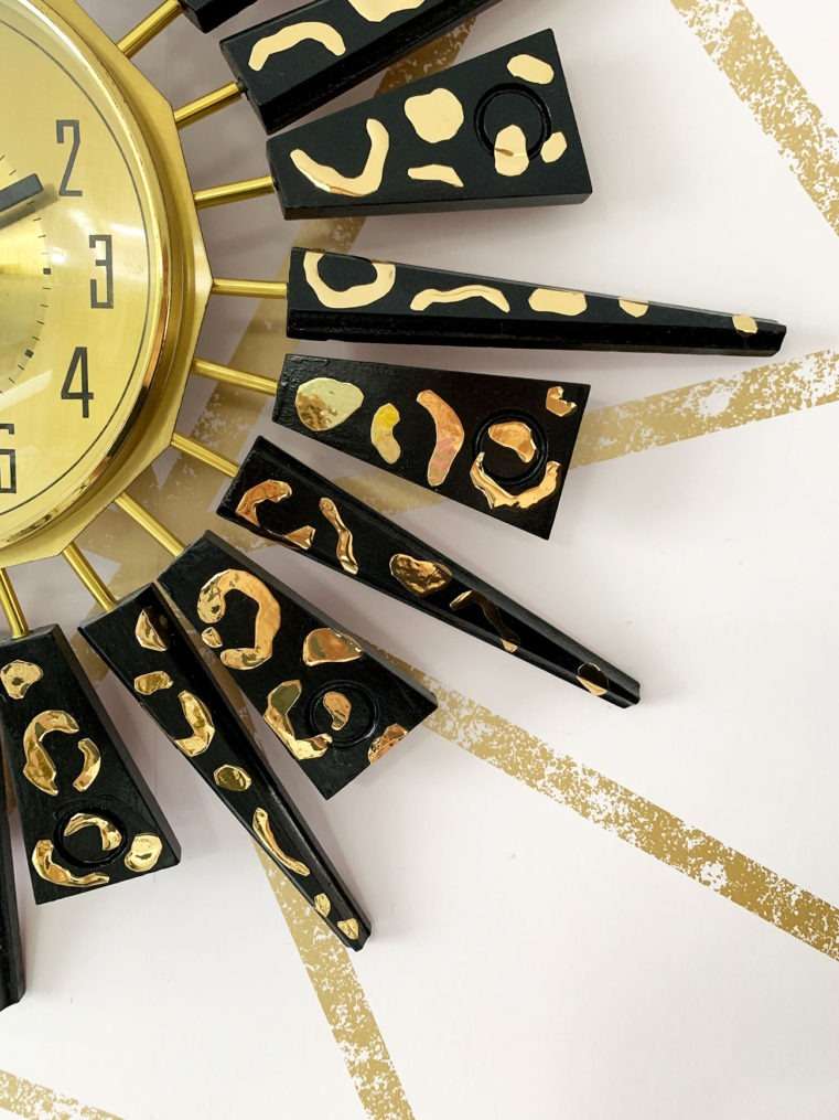 close up of black sunburst vintage clock with gold leopard print decor on a blush and gold wall.