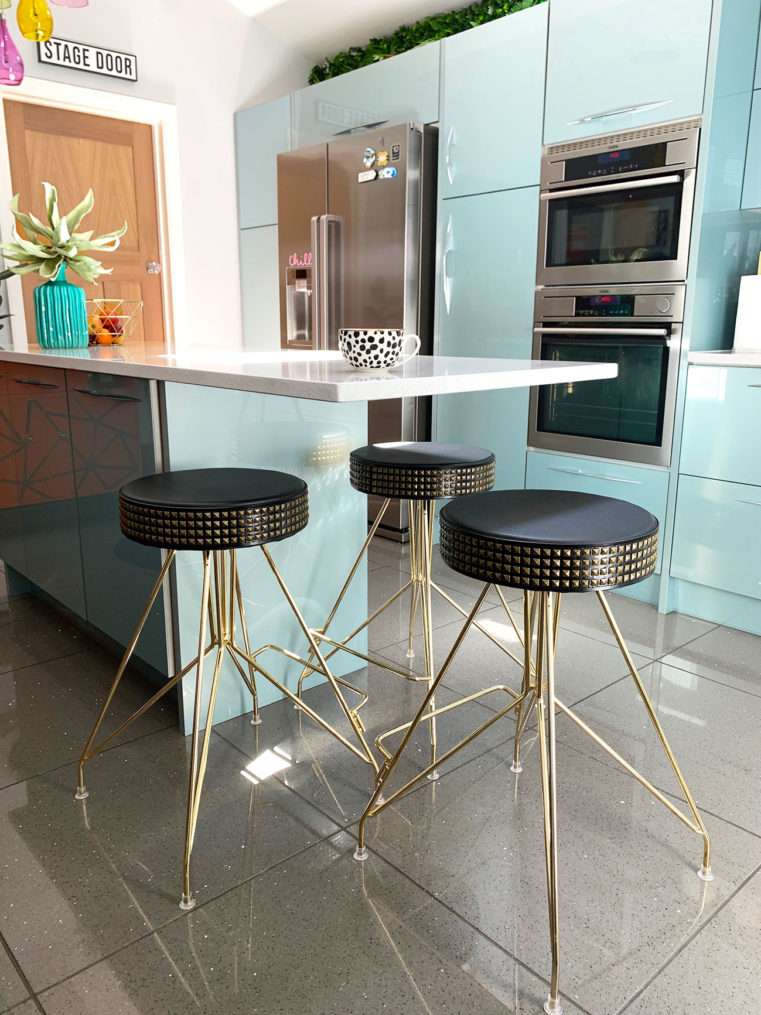kitchen island with gold and black studded stools and mug on quartz counter top.