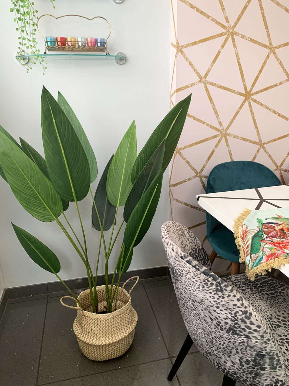 artificial bird of paradise plant in a woven basket at the side of a dining table in a geometric colourfully decorated room.