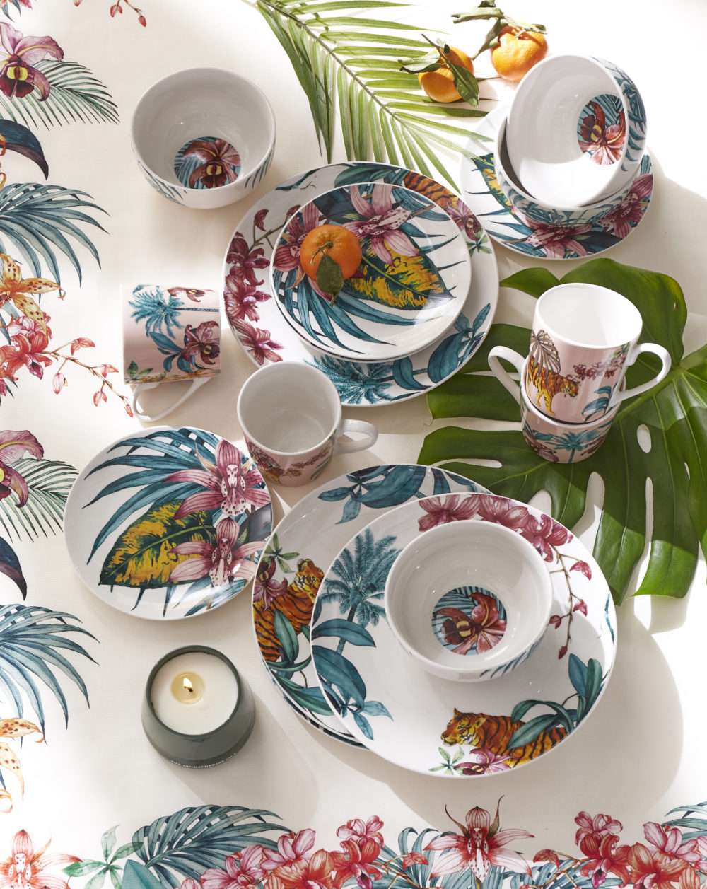 Flatlay table setting with tropical table cloth and tropical plates, dishes and mugs laid on it.