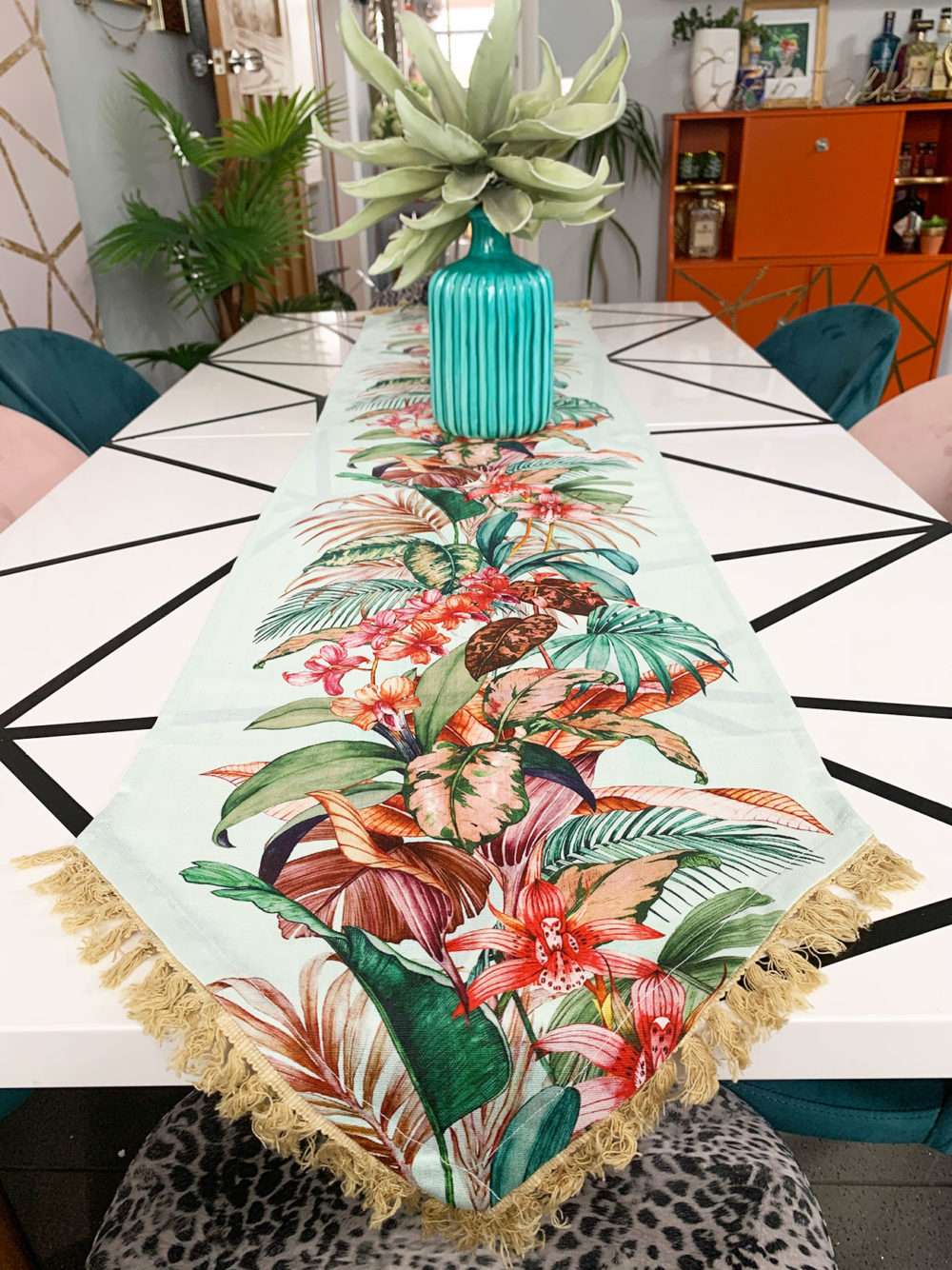 End view of a monochrome geometric dining table with a tropical runner and teal vase.
