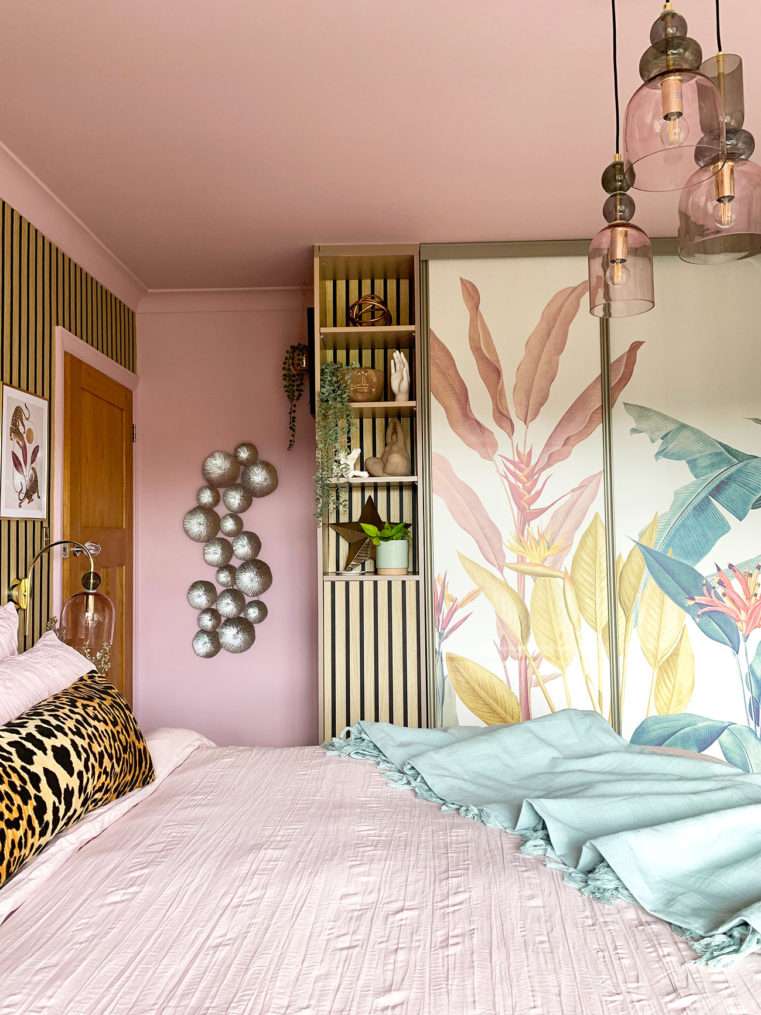 Pink bedroom with tropical mural wardrobe doors, wood slat panel shelves and blush pink bedding.