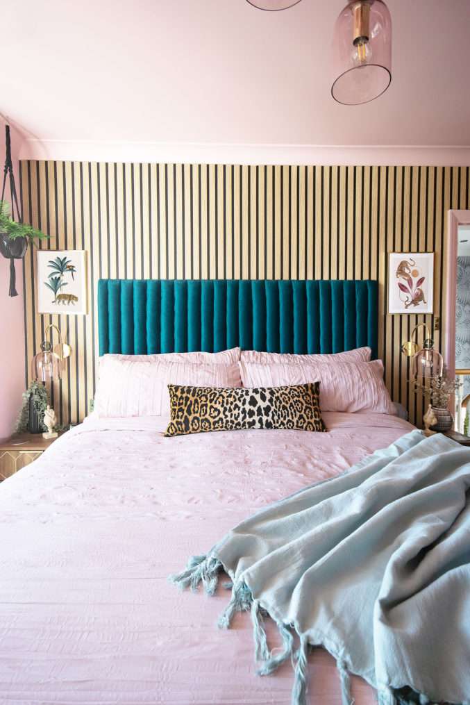 Boutique style bed with blush crinkle bedding, teal velvet headboard, wooden and gold bedside tables, glass and gold wall lights, leopard prints, and panelled wall.