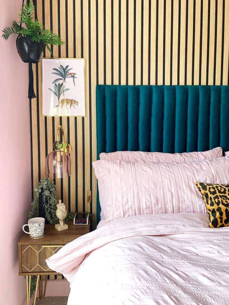 Boutique style bedside with pink and teal decor, leopard wall print, velvet fluted headboard blush glass and gold wall light and slat wood wall.