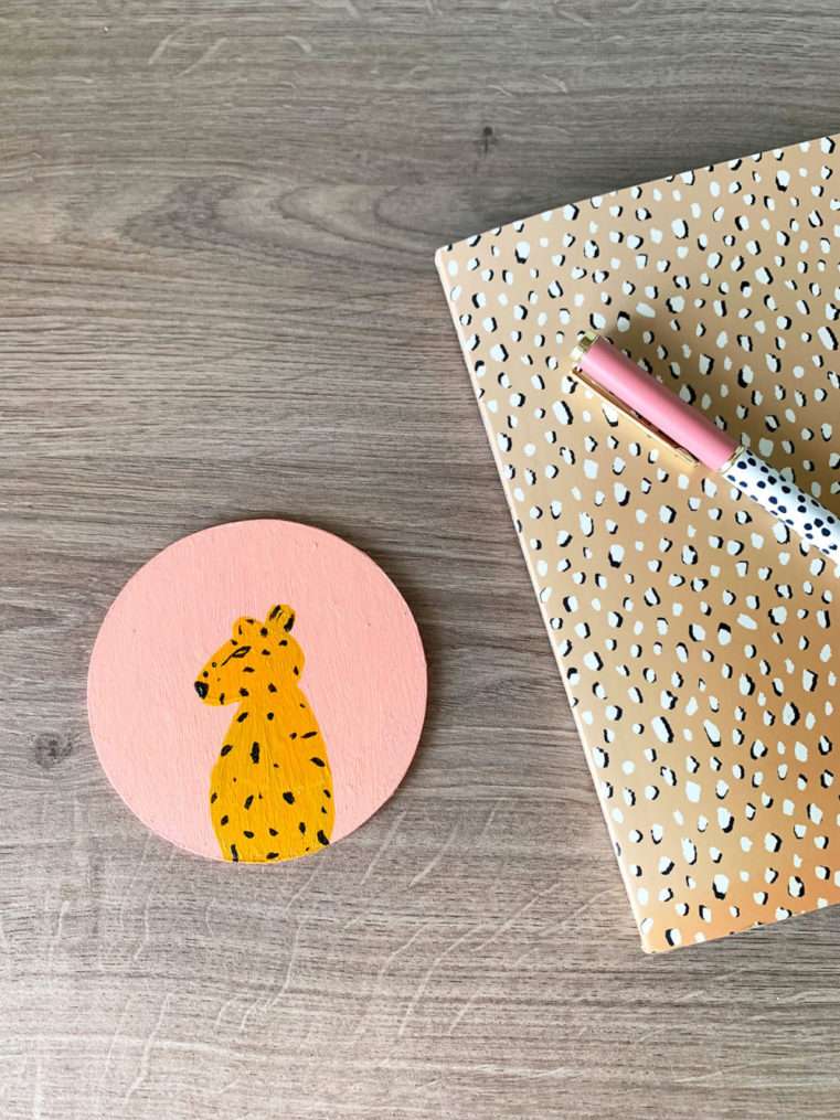 Flatlay of blush coaster with a painted leopard next to leopard print pad and pen.