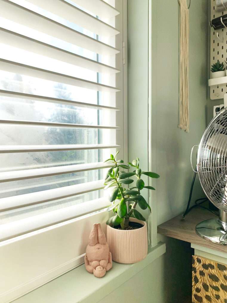Close up of section of plantation shutters with fluted planter and pink yoga sculpture on window sill.