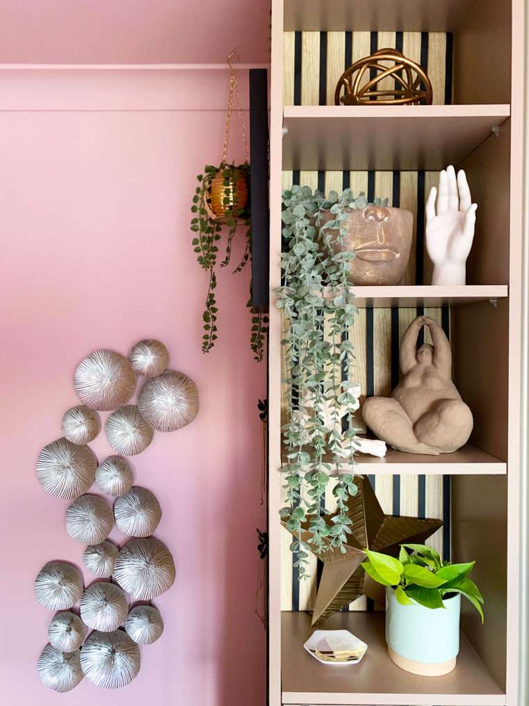 Close up of shelf with quirky sculpture ornaments and pink wall with silver wall art.
