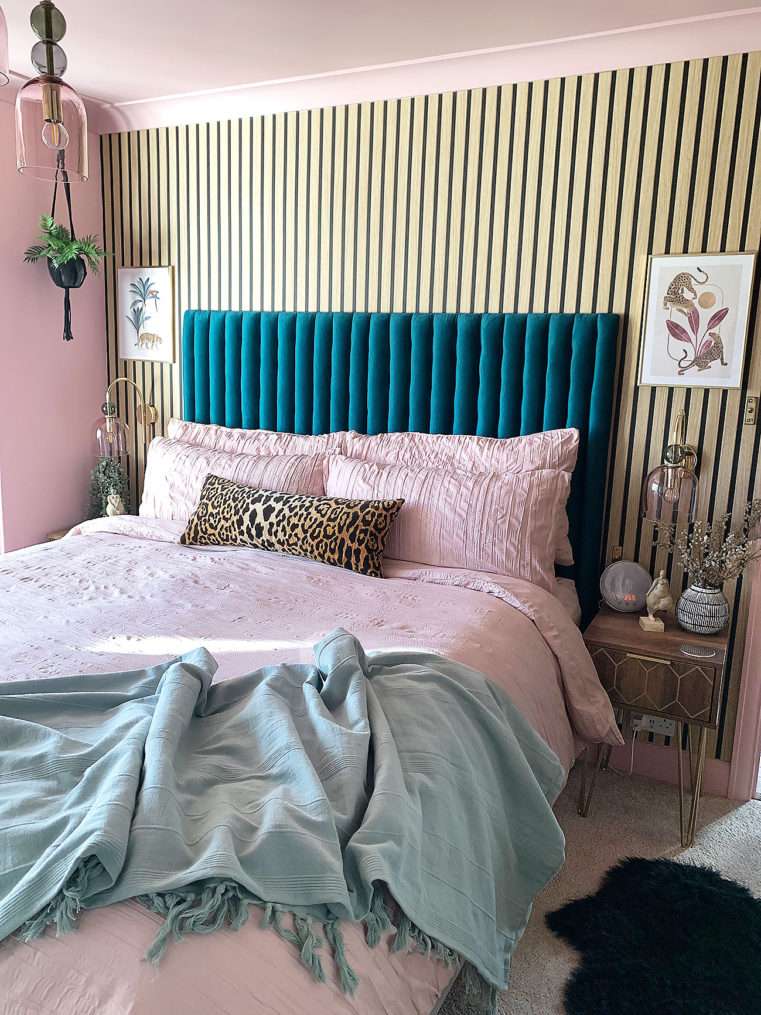 Boutique style bed with blush crinkle bedding, teal velvet headboard, wooden and gold bedside tables, glass and gold wall lights, leopard prints, and panelled wall.