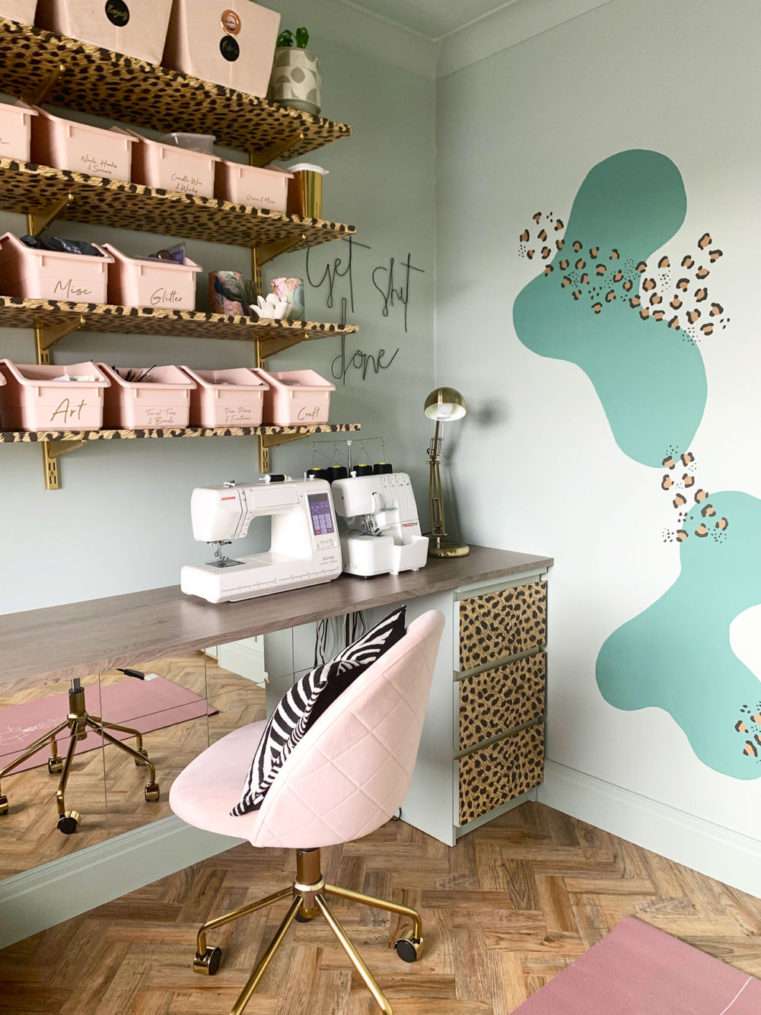 Corner of craft room decorated in soft green, blush, and leopard print with shelves, sewing machine, and swivel chair. Craft & yoga room makeover using calming decor of blush, sage green, teal, and leopard print. Craft corner with storage organisation, sewing machine and desk.
