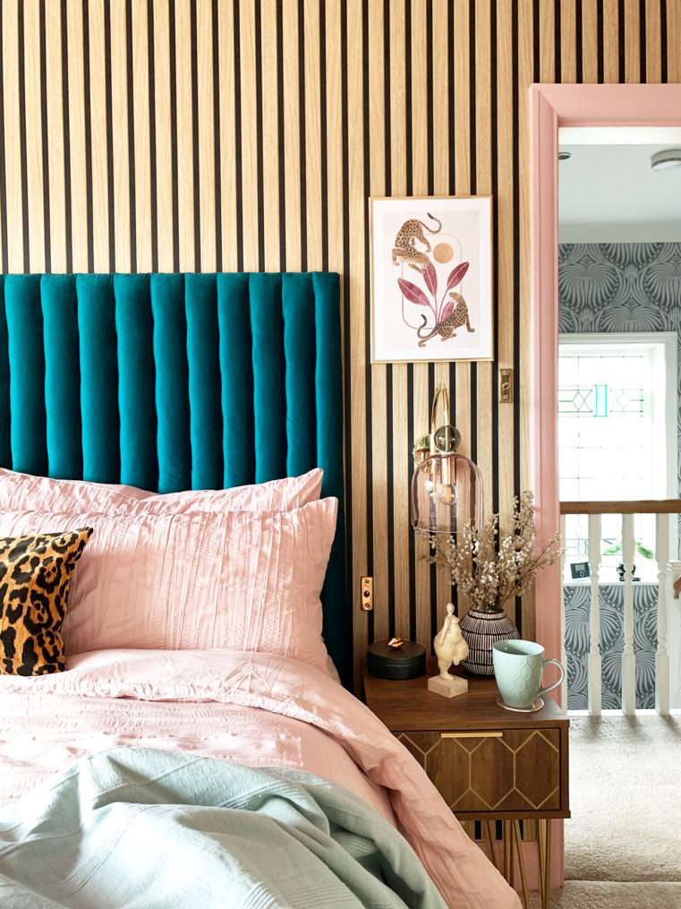Boutique style bedside with pink and teal decor, leopard wall print, velvet fluted headboard and slat wood wall.
